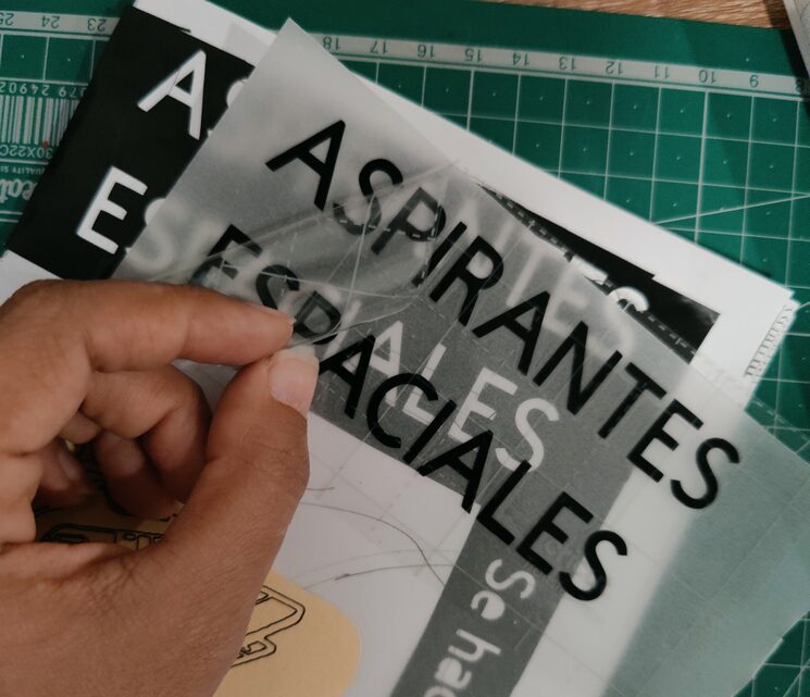 Mano trabaja con un vinilo que dice Aspirantes espaciales, parece estar pegándolo en algún lado