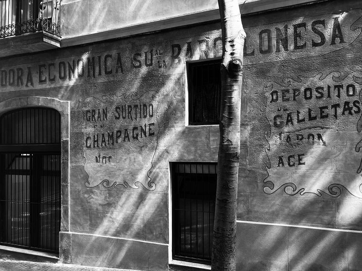 Presente y pasado del tejido artístico del Poble-Sec. Una de las imágenes que compondrán la "sección histórica" del volumen "Poble Sec Col-lectiva": Porción frontal de una planta calle en Carrer Margarit con decoraciones publicitarias de principios de 1900, arriba del Parallel. Julio 2025, Autores Col-lectiva.