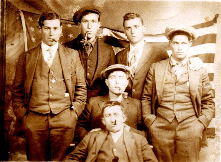 Uns joves de Tàrbena fotografiats cap al 1920, ben elegants, fumant puros i lluint rellotges de cadena. Darrere, la bandera americana. Volien retratar el seu èxit. Foto cedida pel Centre d