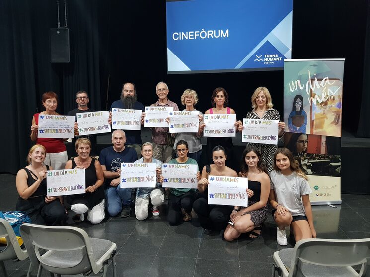 Fotografía de los espectadores del Festival Transhumant apoyando el proyecto con carteles con un mensaje entre las etiquetas #UnDiaMés #SuperarElBullying